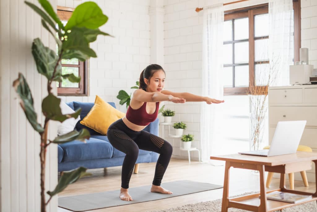 Young Asian woman performs a squat in her living room.